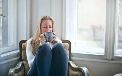 A woman is sitting in a chair drinking a cup of coffee.