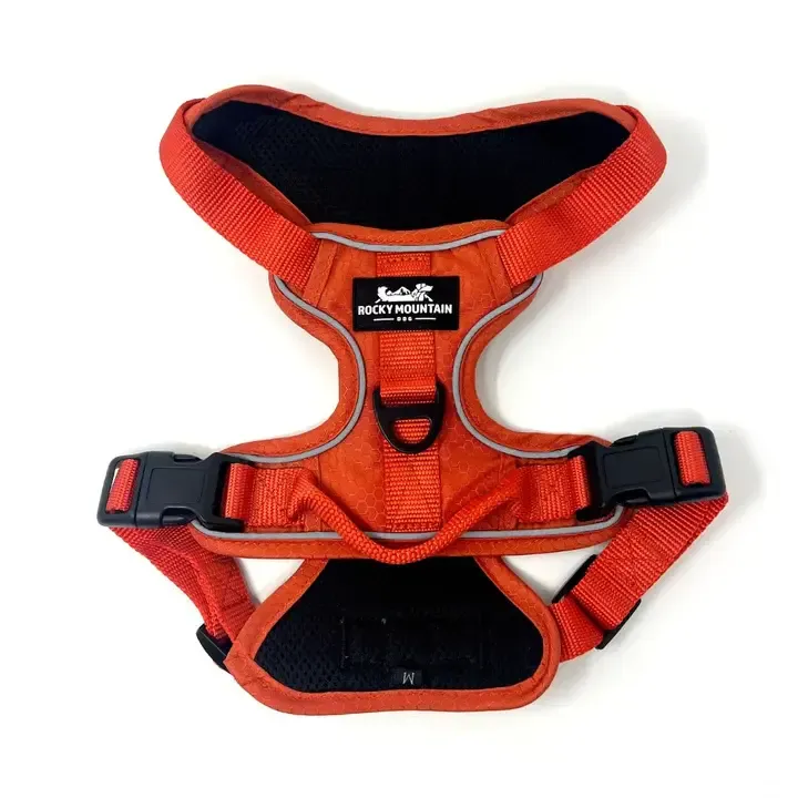 A Rocky Mountain Dog Summit All-Terrain Harness in orange, displayed against a neutral background, highlighting its front and back leash clips, control handle, reflective trim, and adjustable straps for a secure fit.