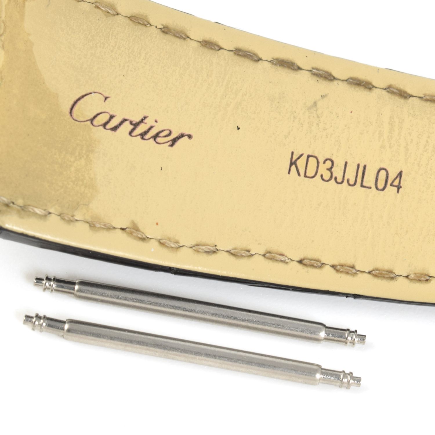 Two stainless steel spring bars placed below a beige leather Cartier watch strap stamped KD3JJL04, compatible with Calibre de Cartier 42mm models