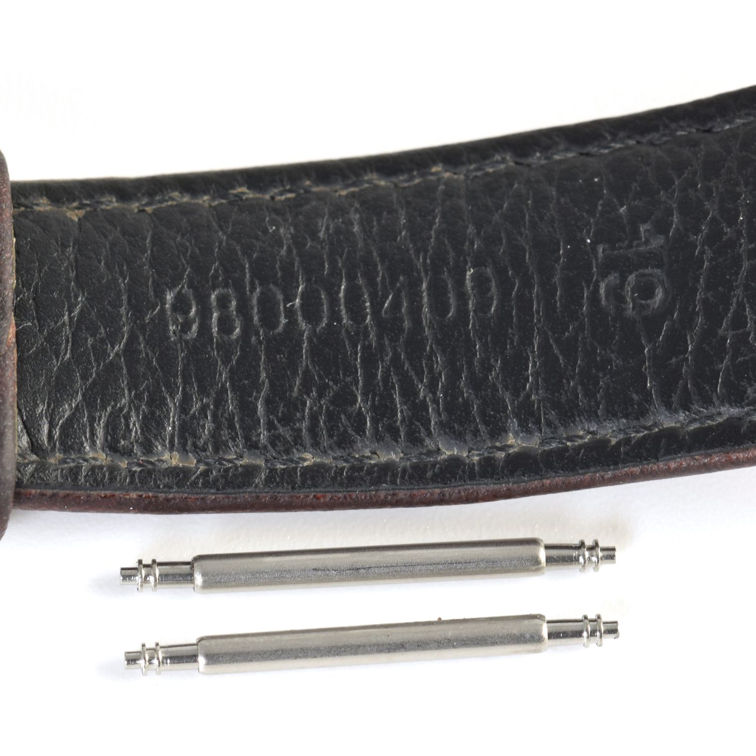 Two stainless steel spring bars placed below a black Omega Speedmaster Moonwatch leather strap stamped 98000409, shown on a white background.