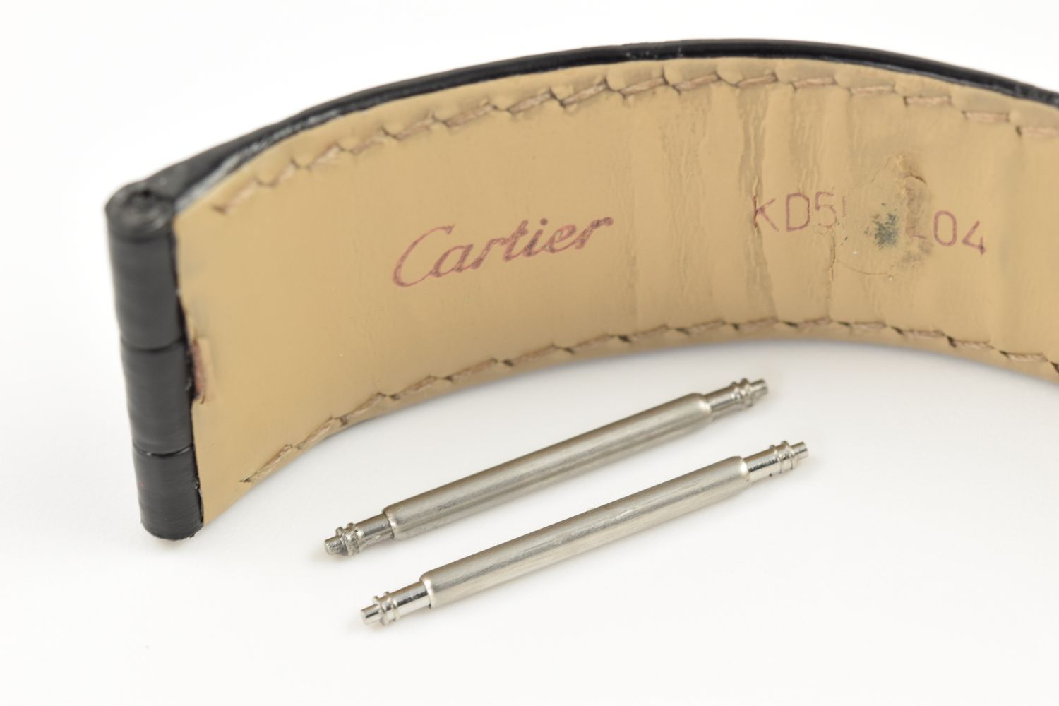 Two stainless steel spring bars placed below a beige leather Cartier strap stamped KD5...L04, compatible with Cartier Tank Solo 3169 watches