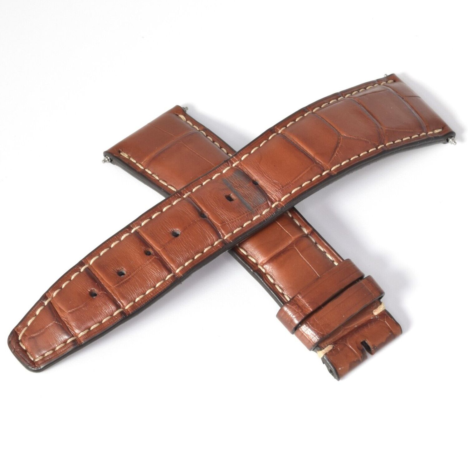Authentic IWC brown alligator leather watch strap with white stitching removed from a Portofino model shown with both pieces crossed and visible wear near the buckle holes and tip, measuring 21mm at the watch end and tapering to 18mm
