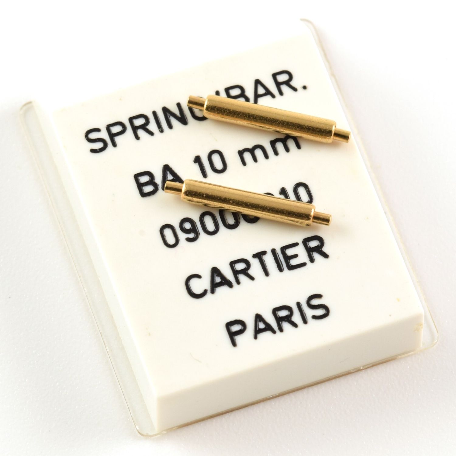 Two gold plated Cartier spring bars resting on original white packaging printed with SPRING/BAR. BA 10 mm 09000010 CARTIER PARIS