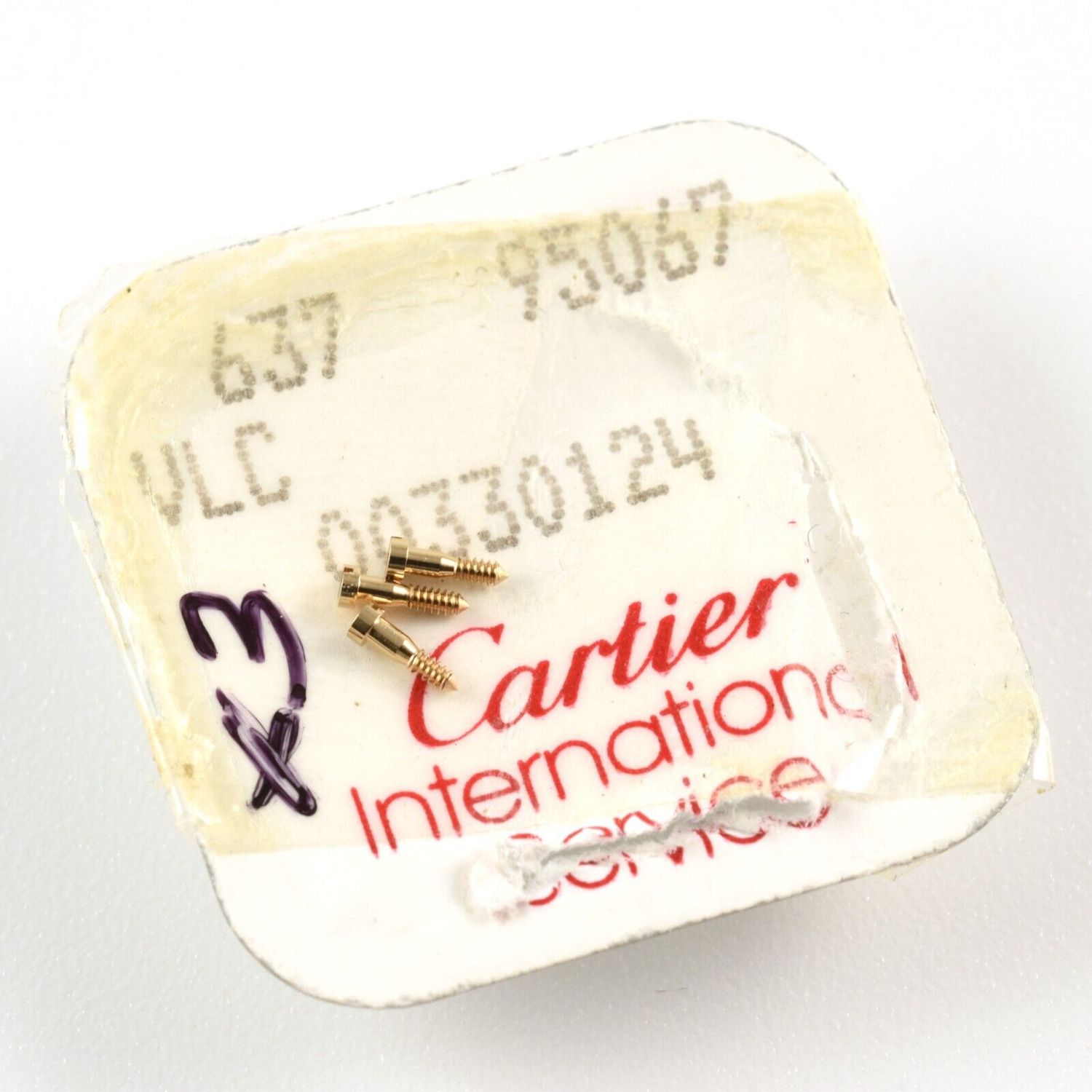 3 gold-plated Cartier lug bar screws resting on opened original service card with printed text 637 95067 VLC 00330124 Cartier International Service and handwritten 3x