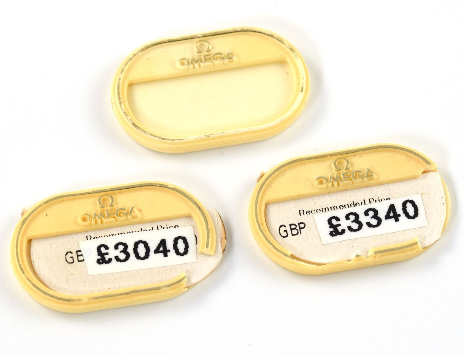 three yellow Omega swing tags with embossed Omega logos and visible GBP price stickers of £3040 and £3340 shown from the front