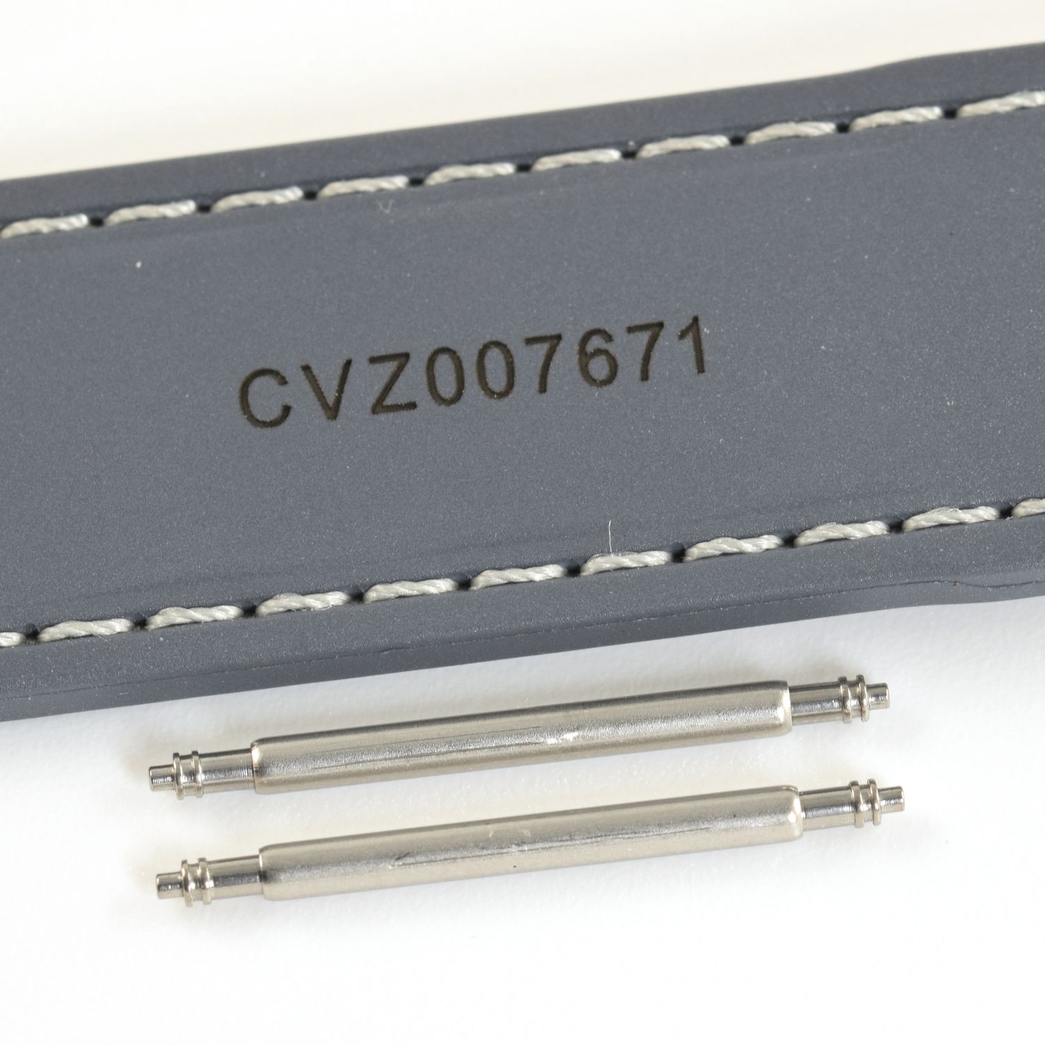 two stainless steel spring bars shown below Omega Aqua Terra blue rubber watch strap stamped CVZ007671 with white stitching on white background