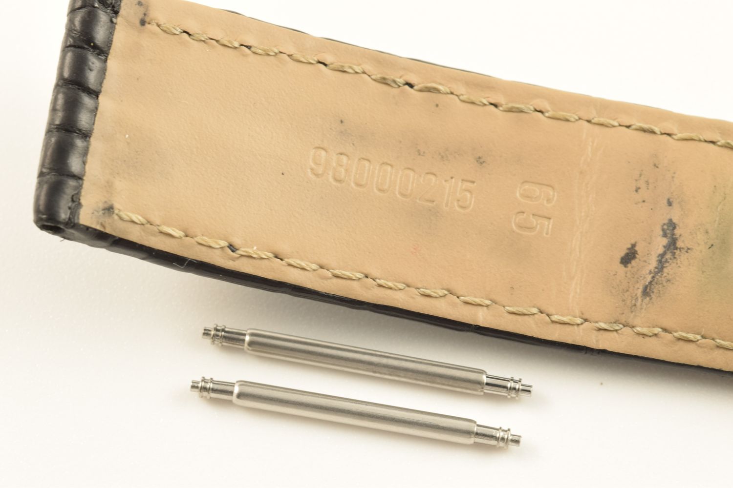 two stainless steel spring bars shown below Omega De Ville Prestige leather strap stamped 98000215 and 65 on beige underside with visible stitching