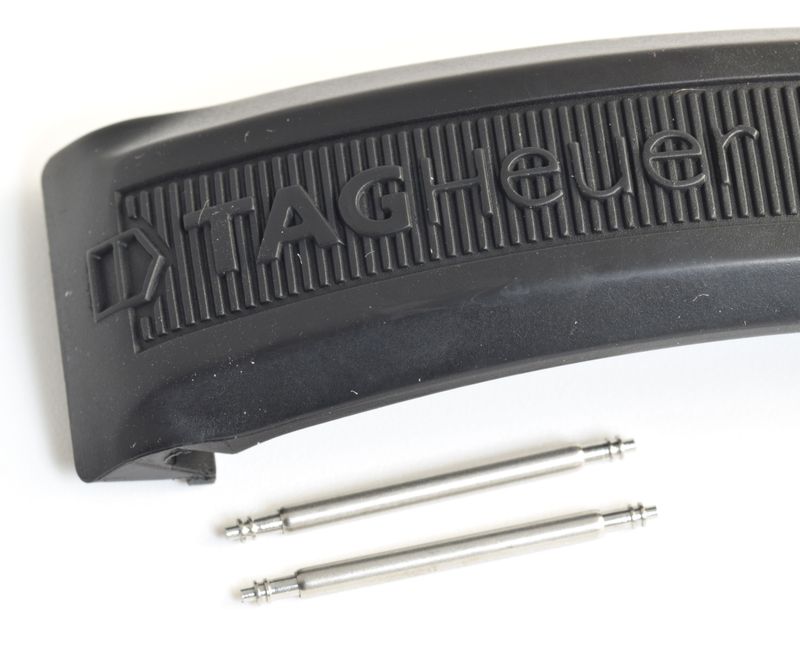 two stainless steel spring bars shown below black TAG Heuer rubber strap with raised TAG Heuer logo and ridged texture on white background