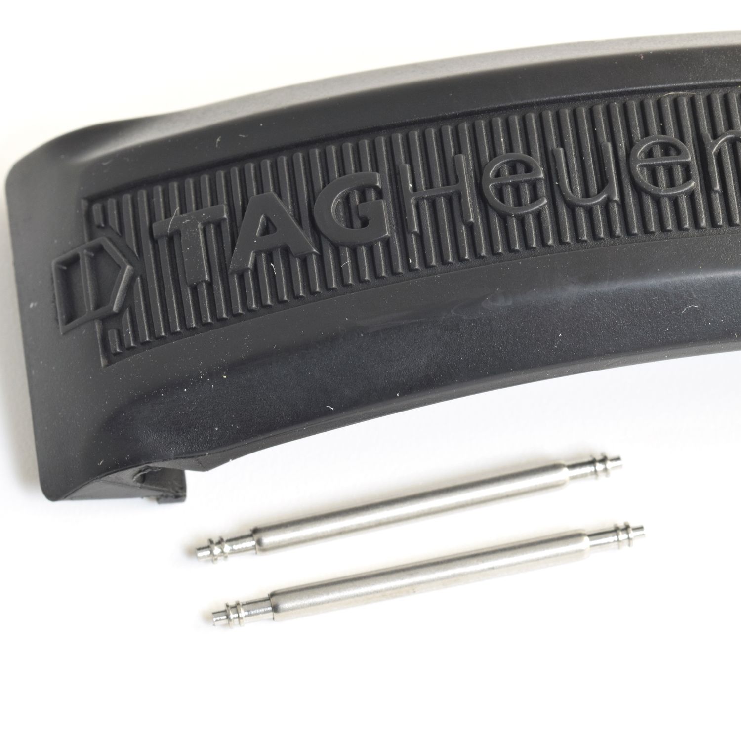 two stainless steel spring bars shown below black TAG Heuer rubber strap with raised TAG Heuer logo and ridged texture on white background