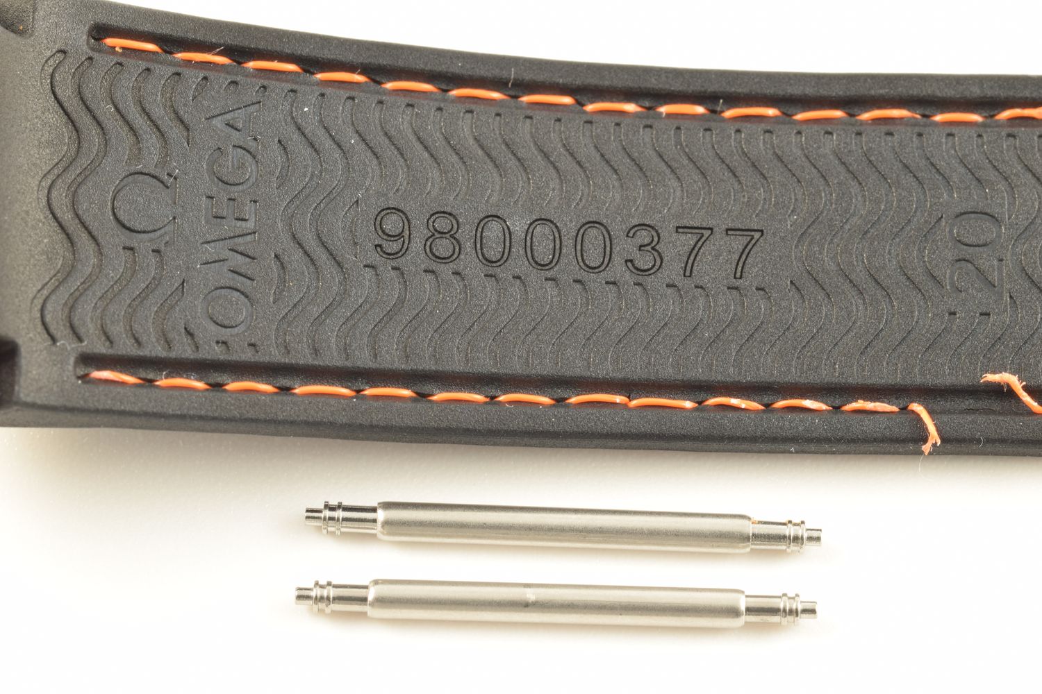 two stainless steel spring bars shown below Omega Planet Ocean black rubber strap with orange stitching stamped 98000377 and 20 on wave-textured background