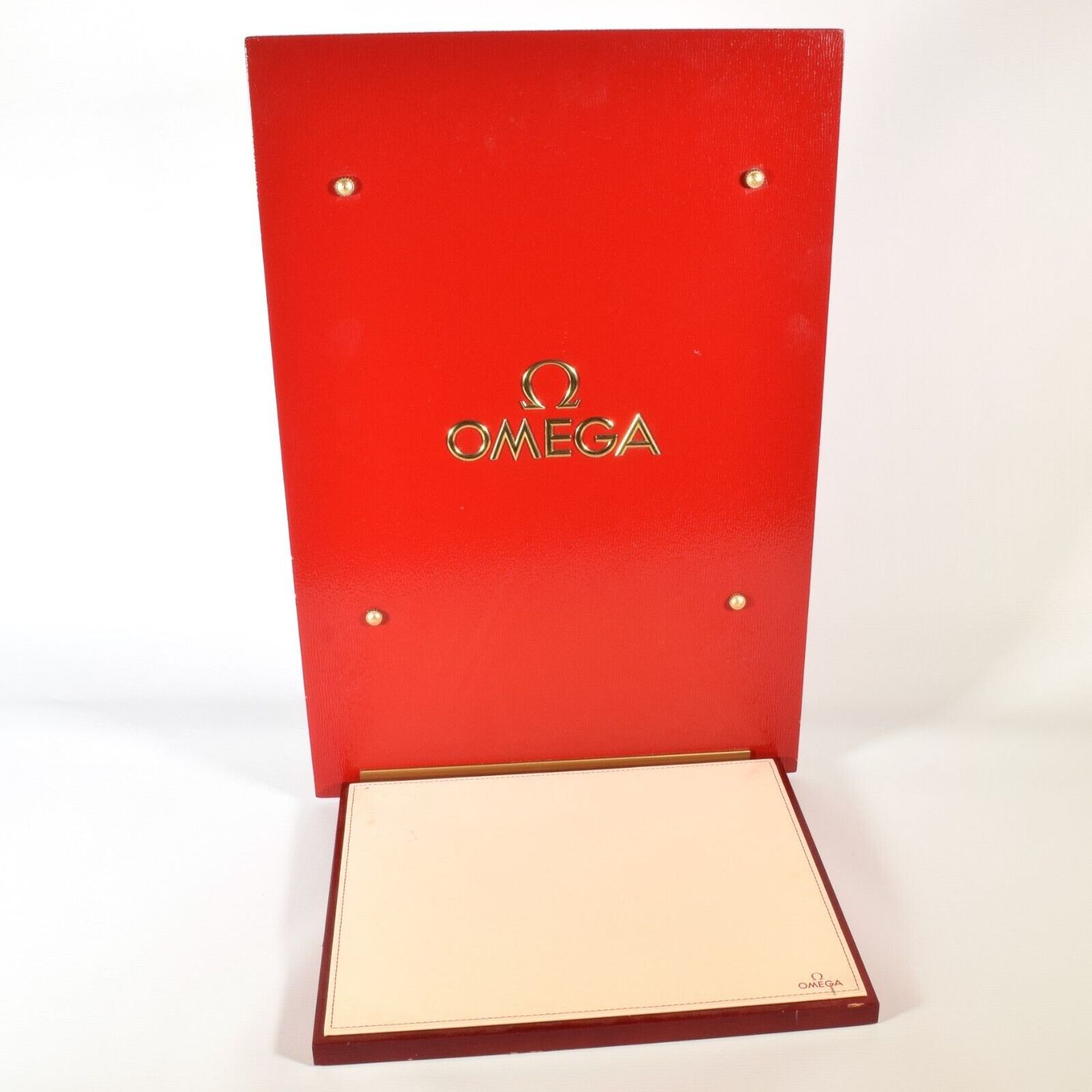 Authentic Omega boutique display stand with red rippled glass upright panel, gold Omega logo, four brass fixings, and attached cream leather tray marked Omega in corner