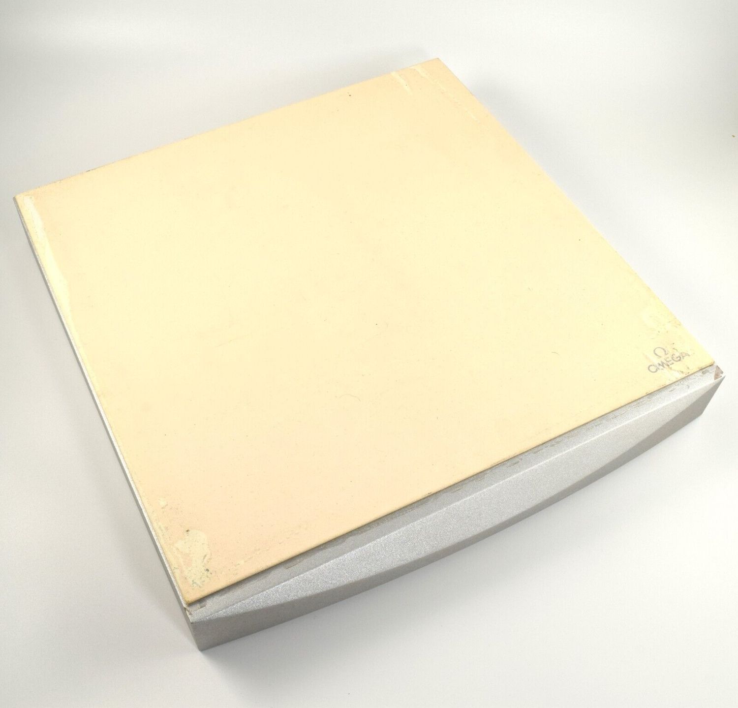 Authentic large Omega watch display tray with cream top surface, missing metal trim, visible tears in corners and small Omega logo in the bottom right