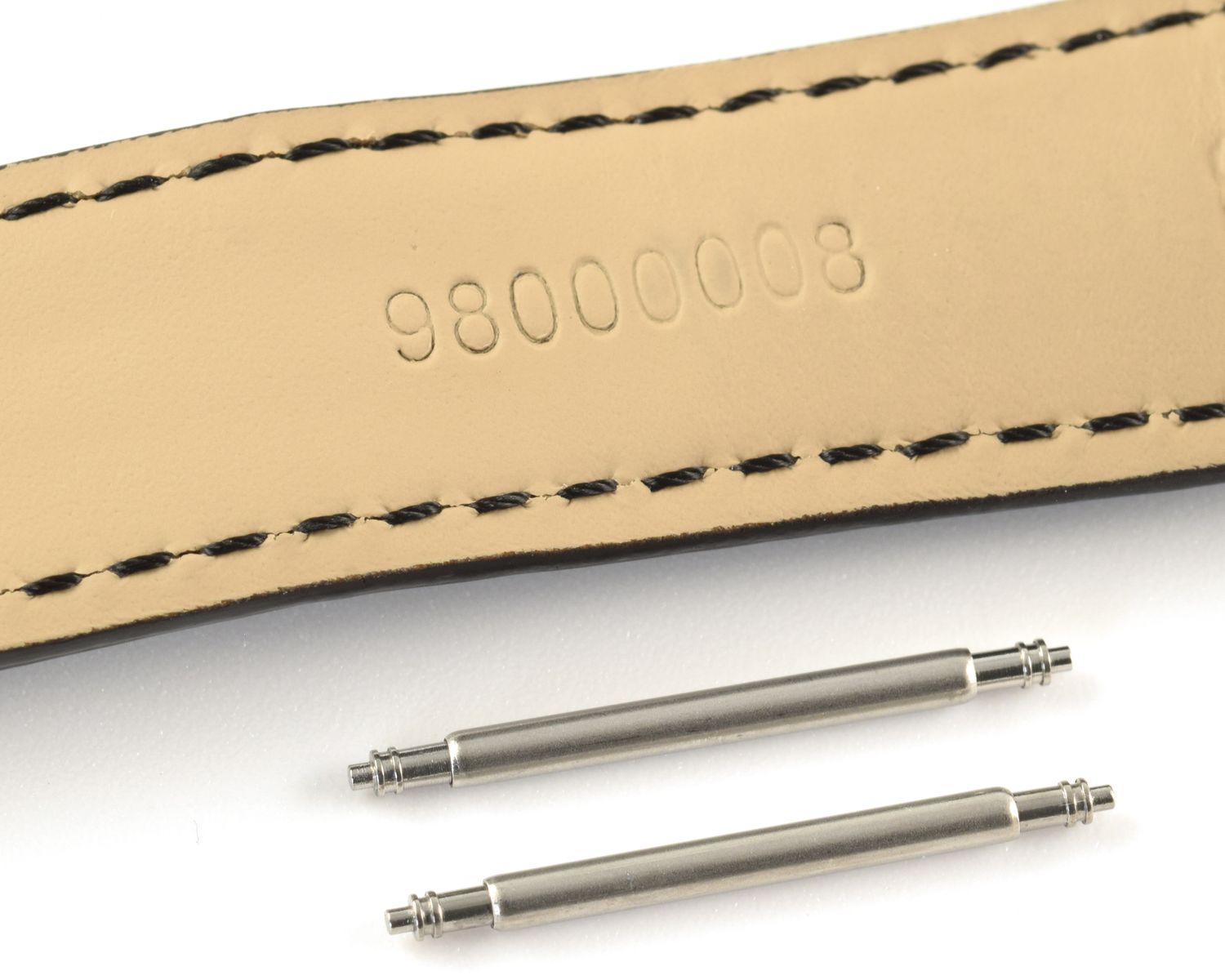 Two stainless steel spring bars placed beneath a black-stitched beige leather watch strap stamped 98000008