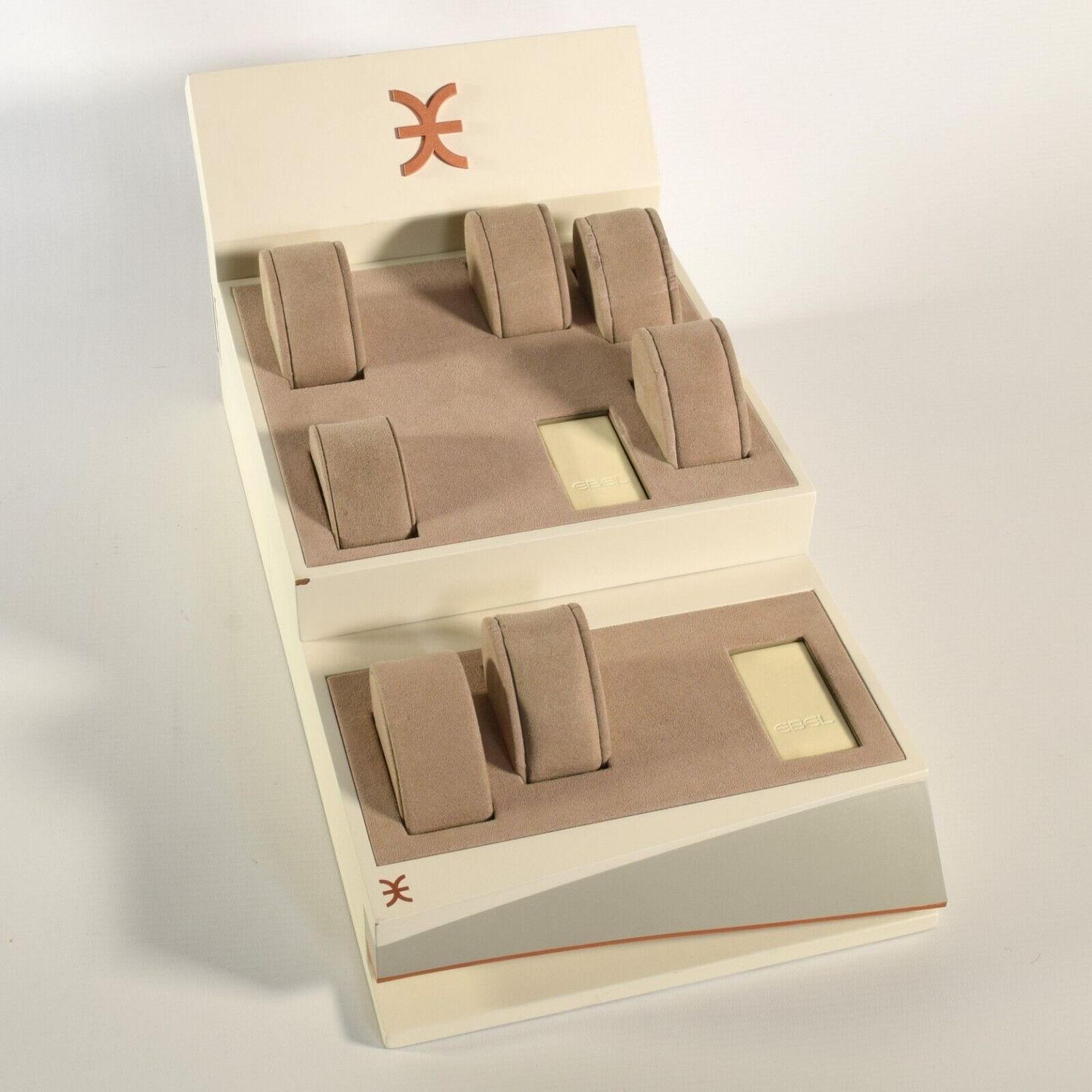 Authentic EBEL cream watch display stand with 7 brown felt watch pillows and 2 EBEL-signed cream plugs shown in a stepped layout with EBEL branding visible on the front and display plates