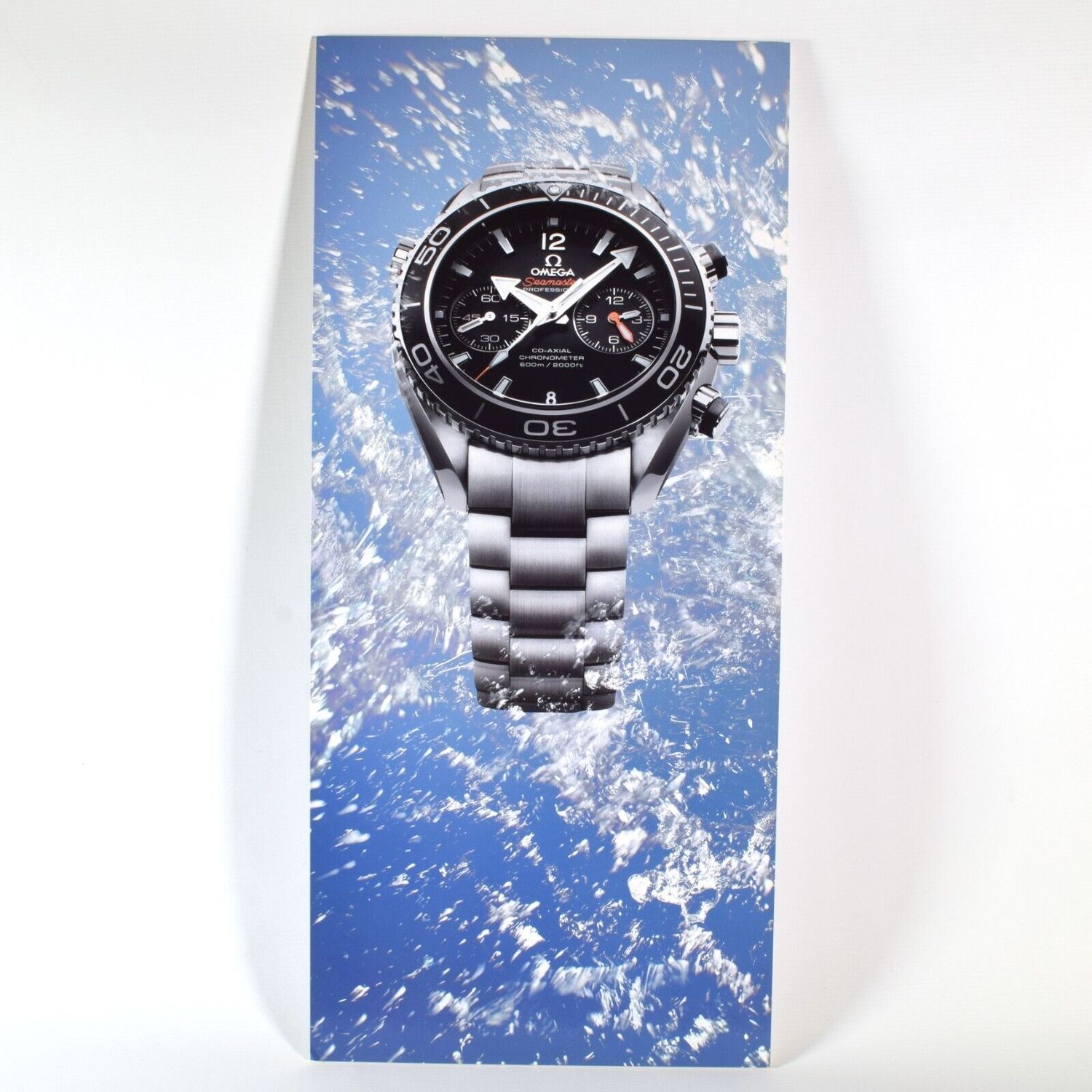 New Omega Seamaster Planet Ocean advertising board showing a stainless steel Planet Ocean watch with black dial and chronograph features emerging through a splash of water against a blue background