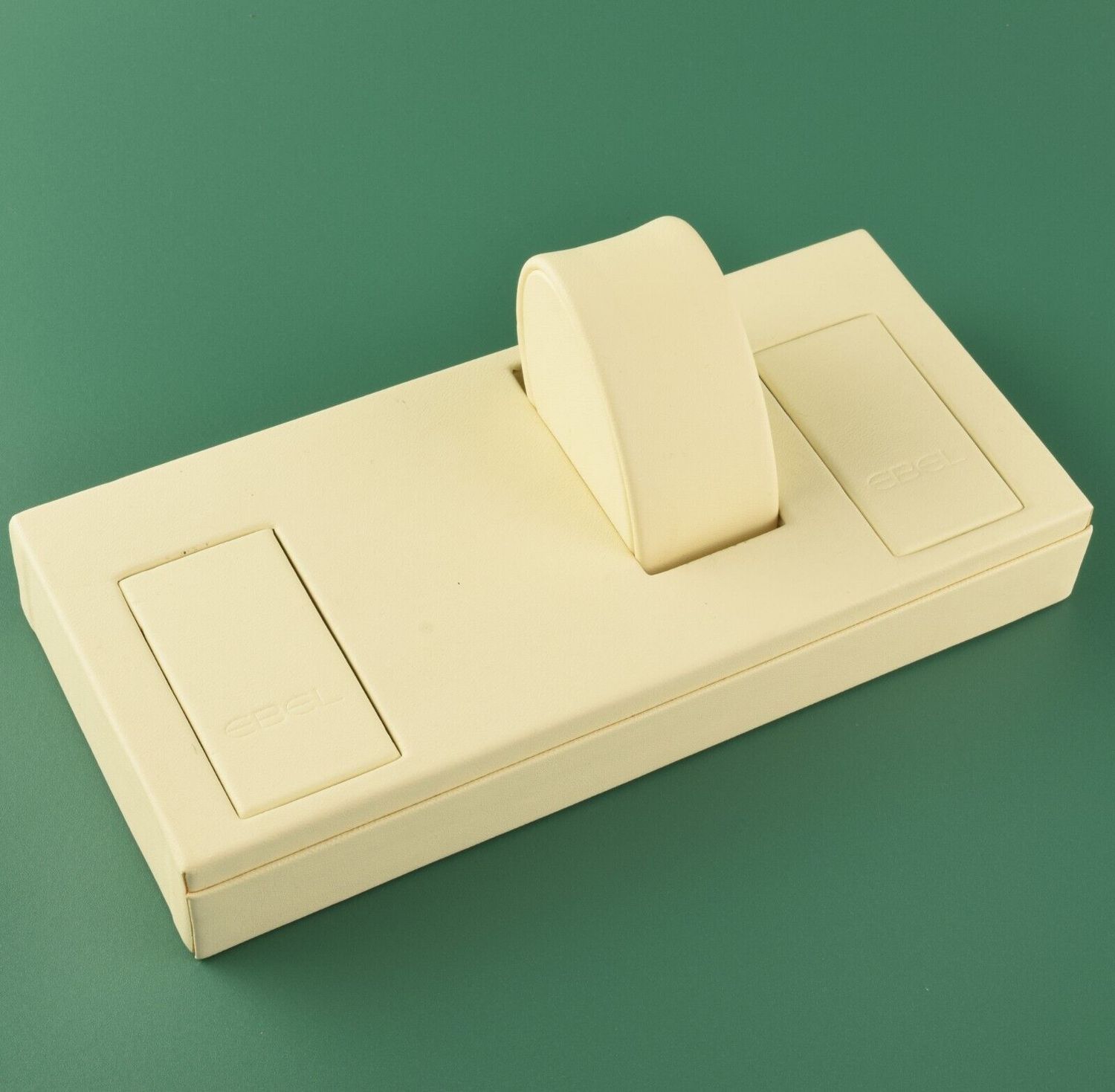 EBEL cream leather watch display tray with one round watch cushion and two EBEL-embossed socket covers on green background