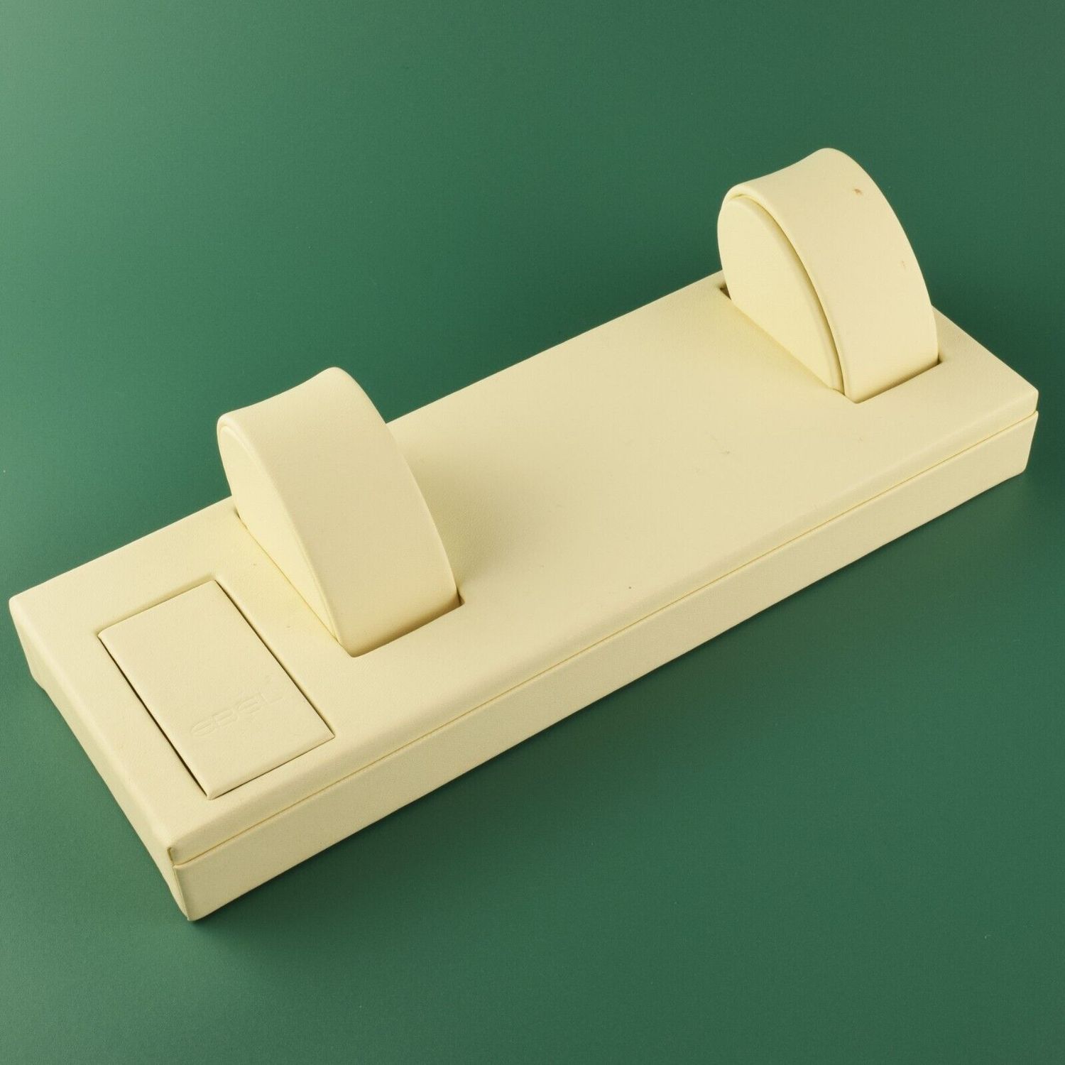 EBEL dealer display tray in cream leather with two round watch pillows and a socket cover on green background