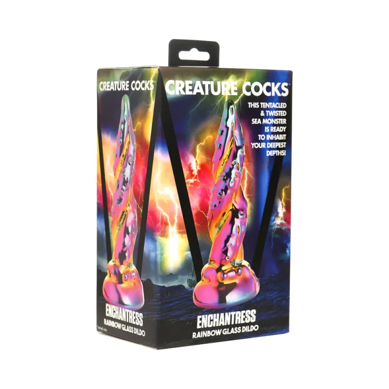 A diagonal view of the Creature Cocks Enchantress Rainbow Glass Dildo, depicted in front of a generic fantasy background. The dildo is a beautiful rainbow oil slick color, resembling two tentacles coiled together.