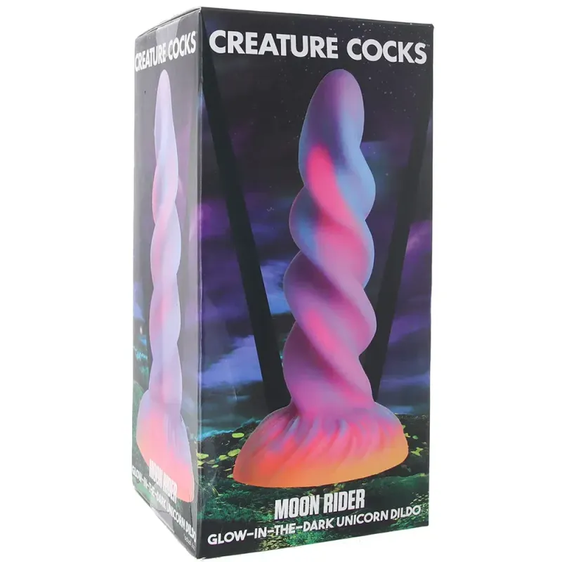 A depiction of the Creature Cocks Moon Rider Unicorn Dildo in its box, depicted in front of a dark fantasy background. The dildo is a pronounced, prominent spiral in the shape of a unicorn horn, poured with an orange base, a pink core, and a blue and purple outer swirl.