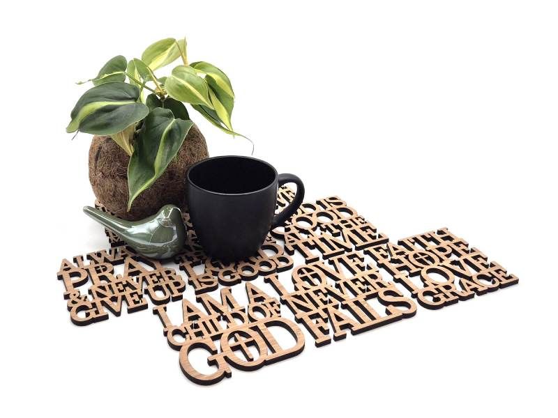 Houten onderzetter met uitgesneden inspirerende woorden, met daarop een zwarte mok, een groene keramische vogel, en een plant