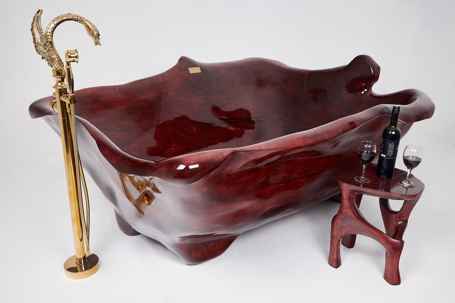 A handcrafted live-edge wooden bathtub carved from a single log, with a gold swan-neck floor-mounte…