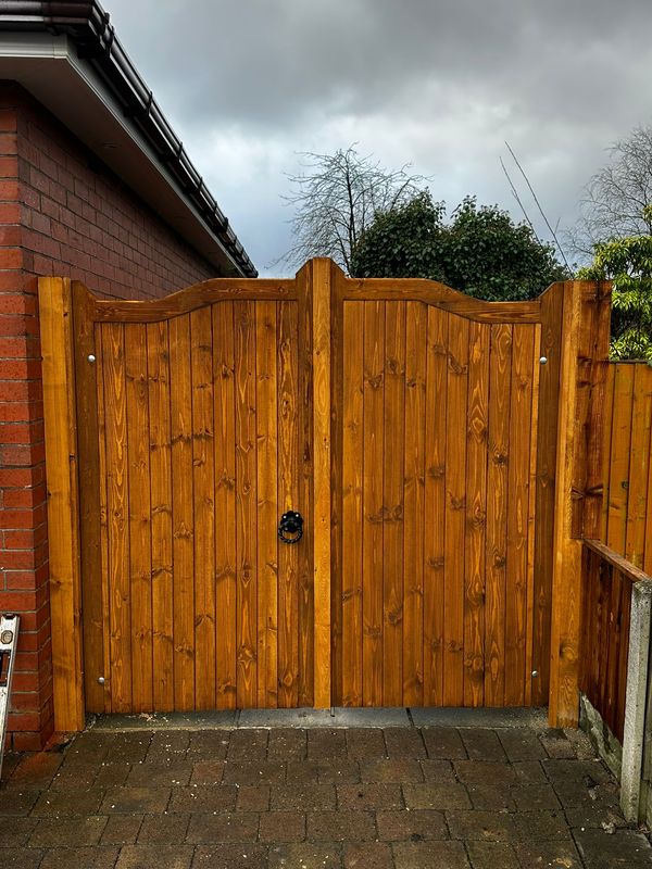 Natural stained Swan Neck double timber gates with black thumb latch, installed between house walls.