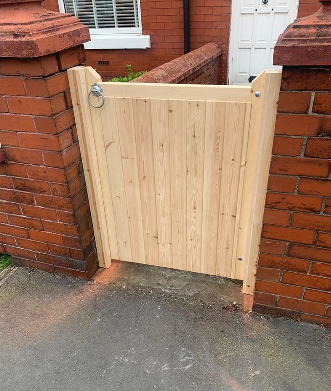 Natural timber tongue and groove garden gate with ring latch, installed between brick pillars.