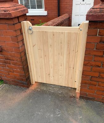Natural timber tongue and groove garden gate with ring latch, installed between brick pillars.