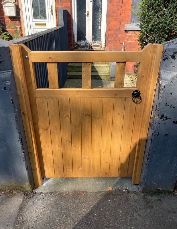 Natural timber garden gate with visible wood grain and ring latch, installed on paved entrance.