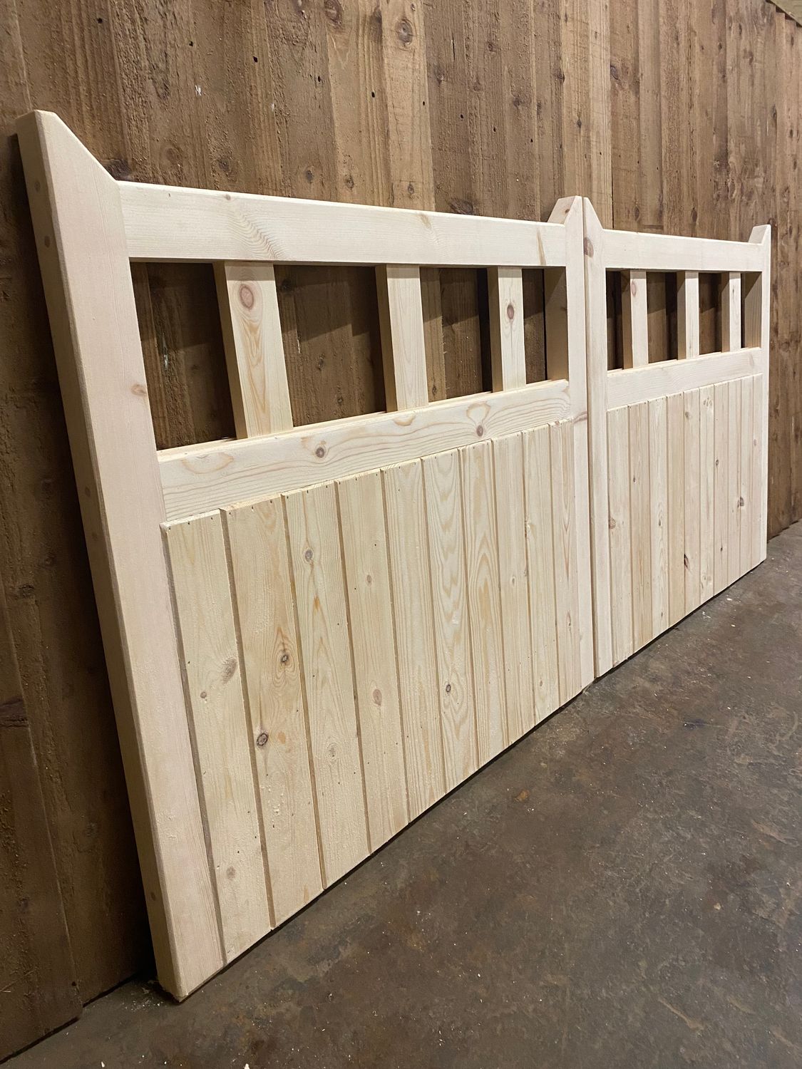 Unpainted wooden driveway gates with vertical cladding and open slatted top section, shown in workshop.