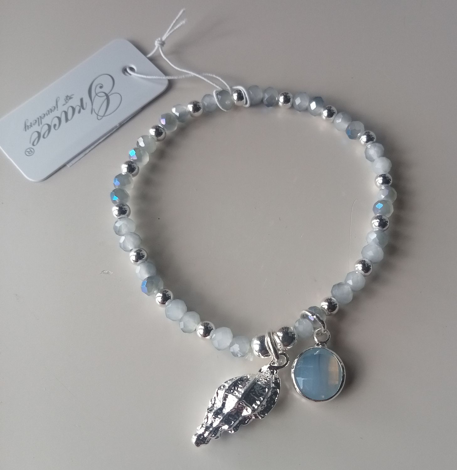 Elasticated blue and silver tone bracelet with a shell charm
