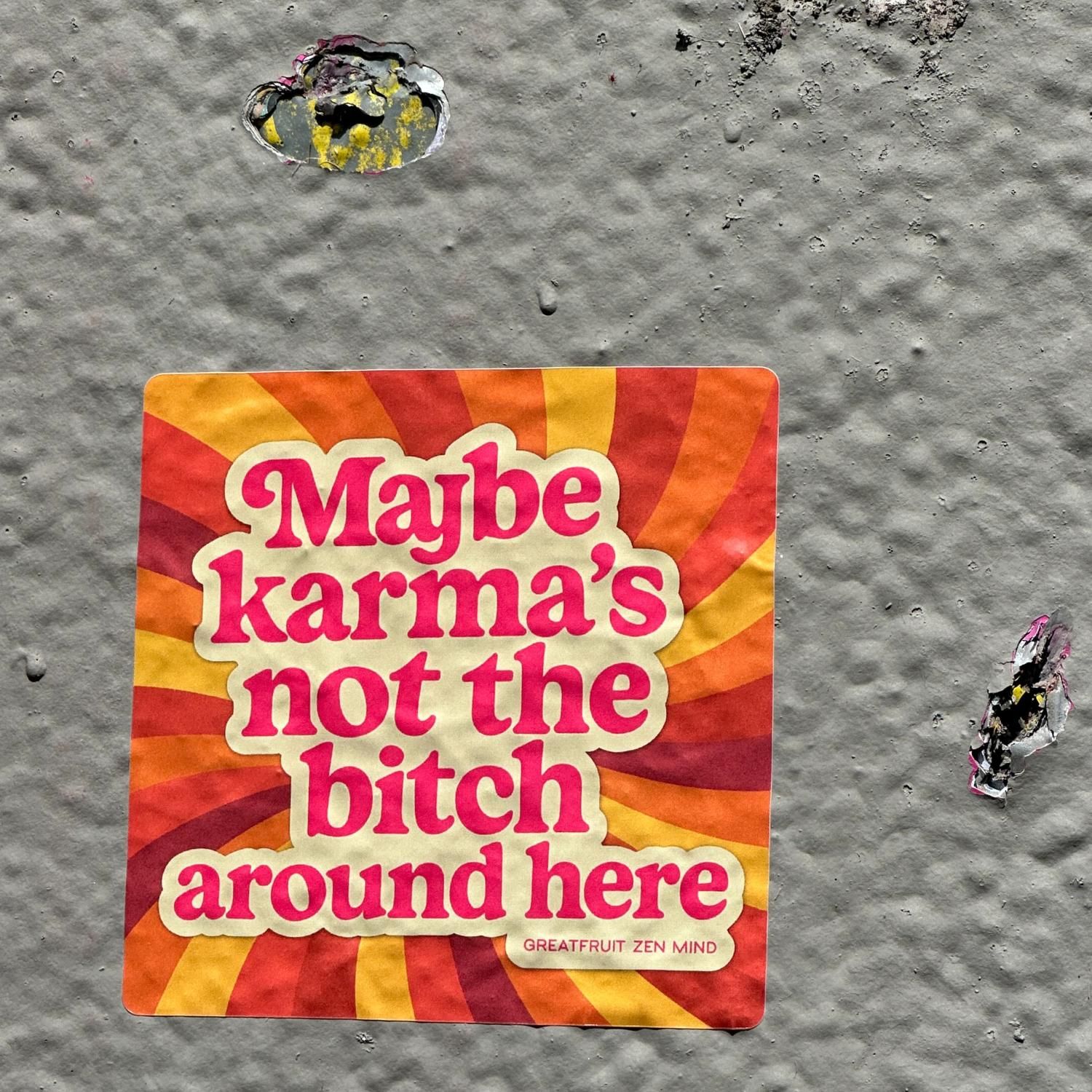 Large Sticker—Maybe Karmas Not The Bitch Around Here. Large 'Maybe karma’s not the bitch around here’ sticker with retro orange swirl background set against concrete wall.