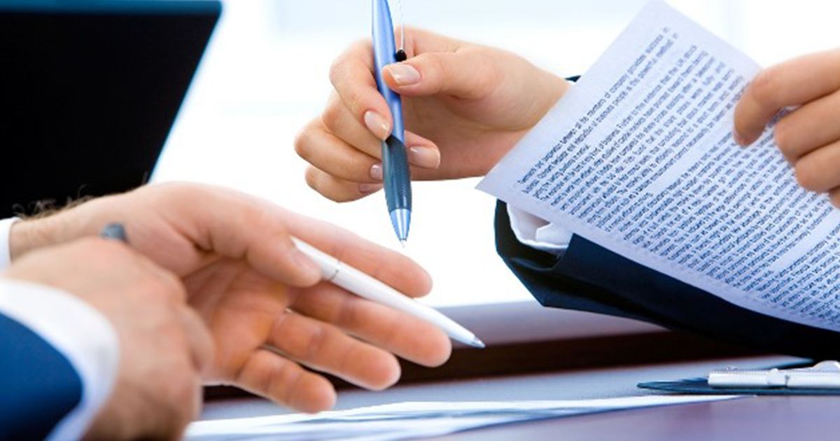 Nahaufnahme von zwei Personen in Businesskleidung, die gemeinsam ein Dokument besprechen und mit Stiften auf den Text zeigen.