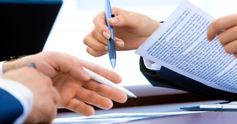 Nahaufnahme von zwei Personen in Businesskleidung, die gemeinsam ein Dokument besprechen und mit Stiften auf den Text zeigen.