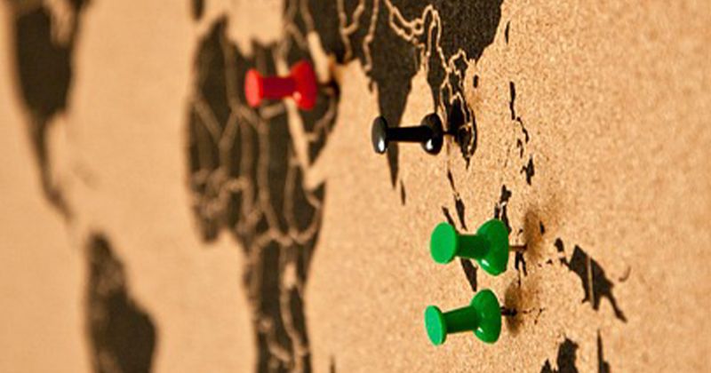 Korkpinnwand mit Weltkarte und bunten Stecknadeln in Asien und Australien.