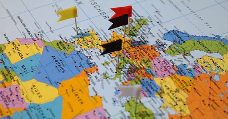 Europakarte mit mehreren kleinen Flaggen in verschiedenen Farben, die Länder wie Deutschland, Spanien und Polen markieren.