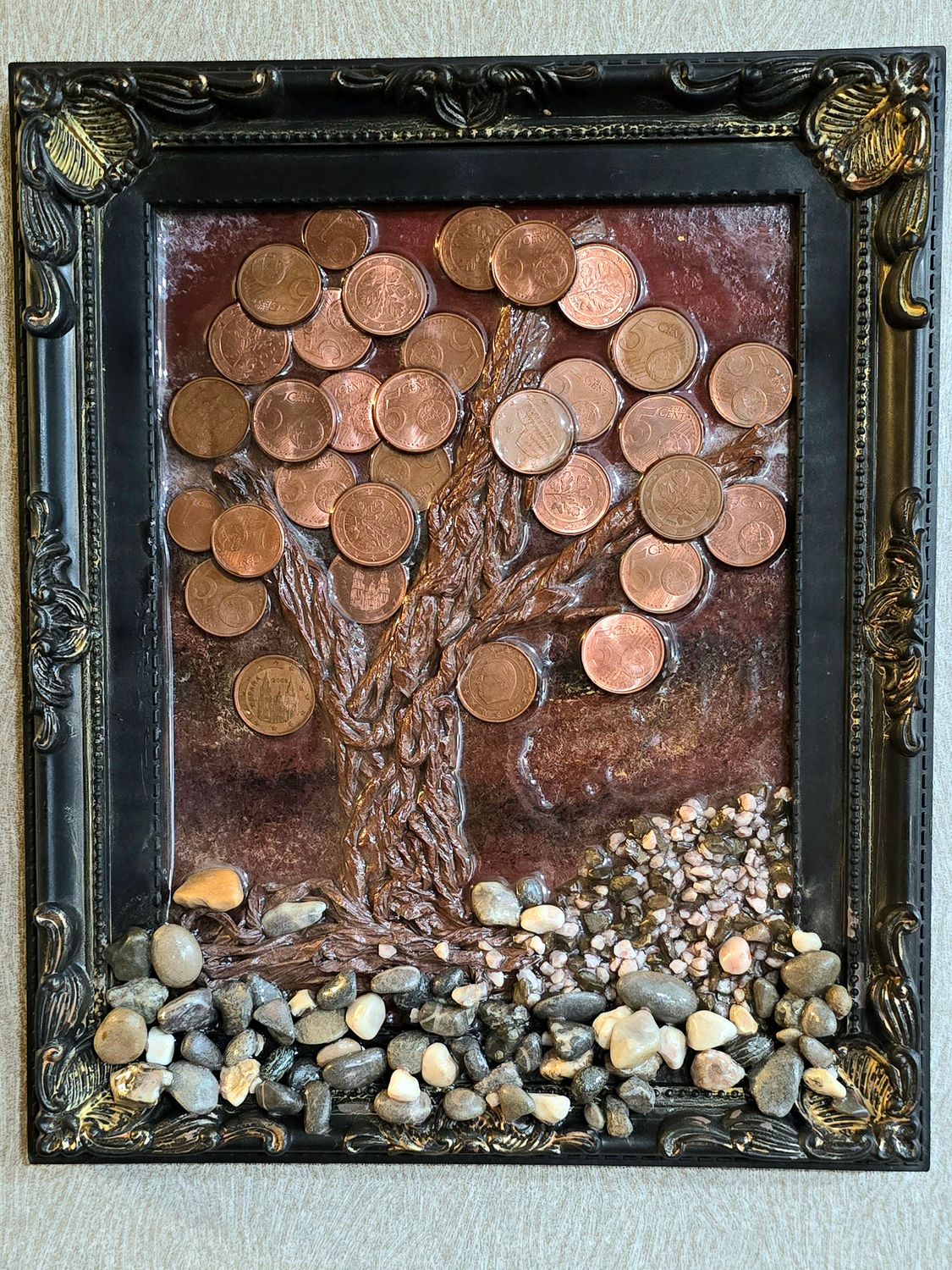 Lucky Coin Tree – Framed Wall Art with Euro Cents and Natural Stones Framed coin tree art made with real euro cents, resin trunk, and pebbles on red background – black and gold vintage frame