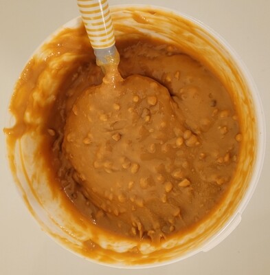Close-up of crunchy peanut butter inside the tub with visible nut pieces – showing thick texture and natural oils.