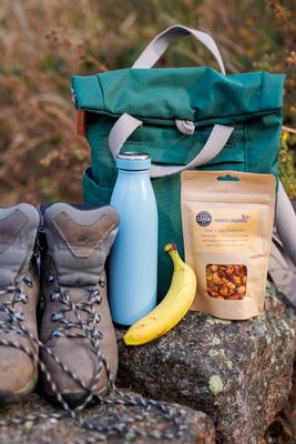 Hungry Squirrel Sweet Spicy Roasted Nuts pouch hiking boots, banana and water bottle – healthy snack for outdoor adventures