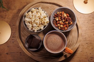 Sweet Aromatic Spiced Nuts served in a bowl alongside popcorn and hot chocolate – a cosy snack pairing for evenings in.