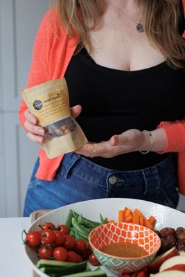 Susan holding the 150g pouch of Sweet & Spicy Roasted Nuts above a colourful salad – a bold topping or snack option.