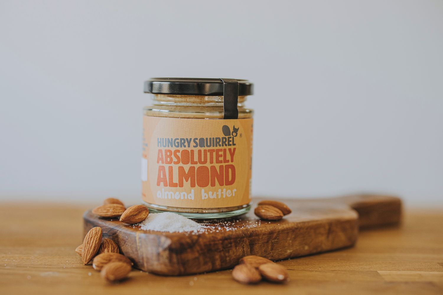 Jar of Absolutely Almond Butter with almonds and sea salt scattered – showing key ingredients.


