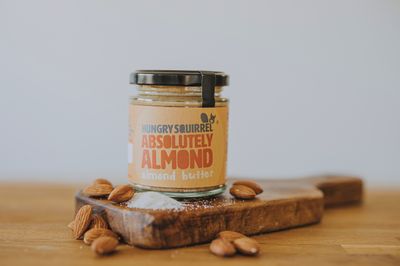 Jar of Absolutely Almond Butter with almonds and sea salt scattered – showing key ingredients.

