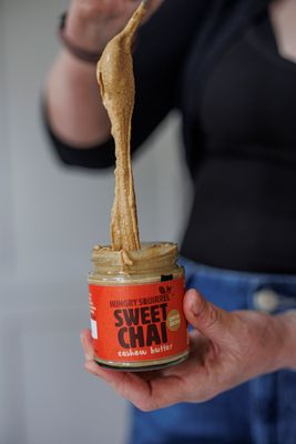 Hand lifting a spoonful of Sweet Chai Cashew Butter from the jar – showing smooth, spoonable texture.