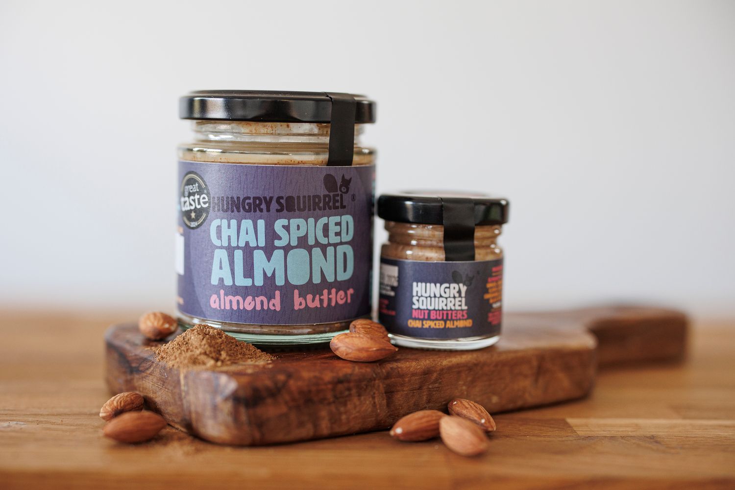180g and 40g jars of Chai Spiced Almond Butter displayed on a wooden board with almonds.