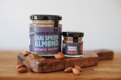 180g and 40g jars of Chai Spiced Almond Butter displayed on a wooden board with almonds.