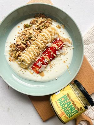 Papaya, Coconut & Pineapple Granola over yoghurt, with sliced banana and fresh raspberries, Peanut Paradise Nut Butter jar.