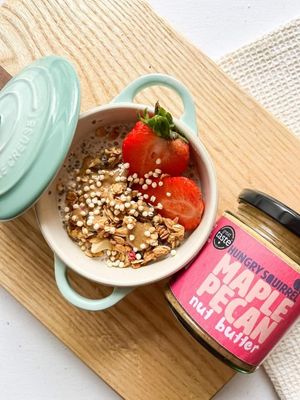 40g Maple Pecan Nut Butter jar beside a bowl of yoghurt topped with granola, fresh strawberries, and seeds.