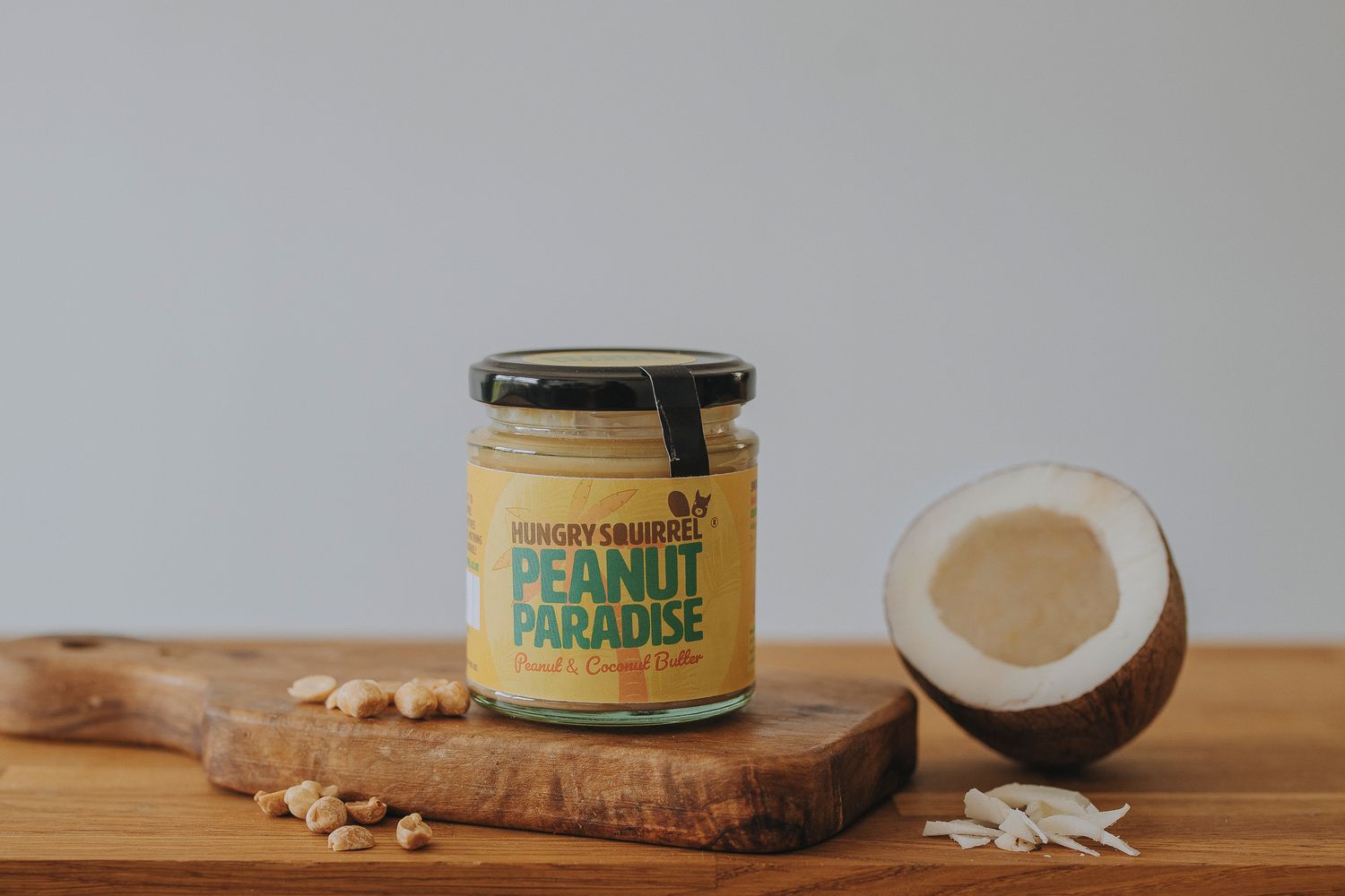 180g Peanut Paradise Nut Butter jar with yellow label on a wooden board, surrounded by coconut pieces.