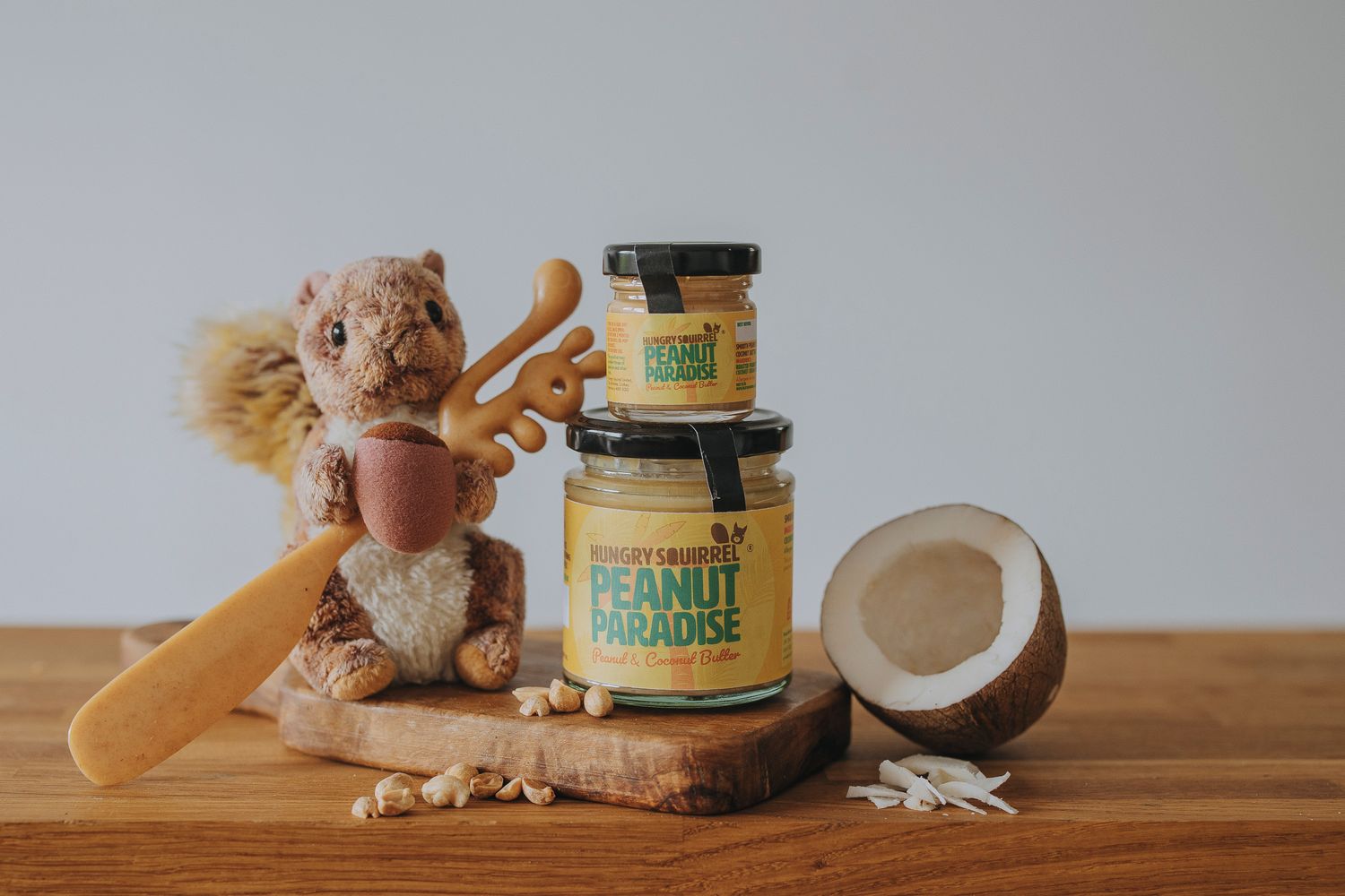 Peanut Paradise Nut Butter jars (180g and 40g) stacked on a wooden surface with peanuts and coconut pieces beside them.